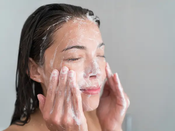 A woman gently applying a cleansing foam to her face representing the initial step in a biological skincare routine for flawless skin