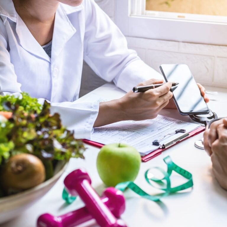 A close up view of a nutritionist in a white coat providing a personalized metabolic wellness consultation using a smartphone to explain a plan alongside fresh green vegetables a green apple and pink dumbbells for physical activity resistance