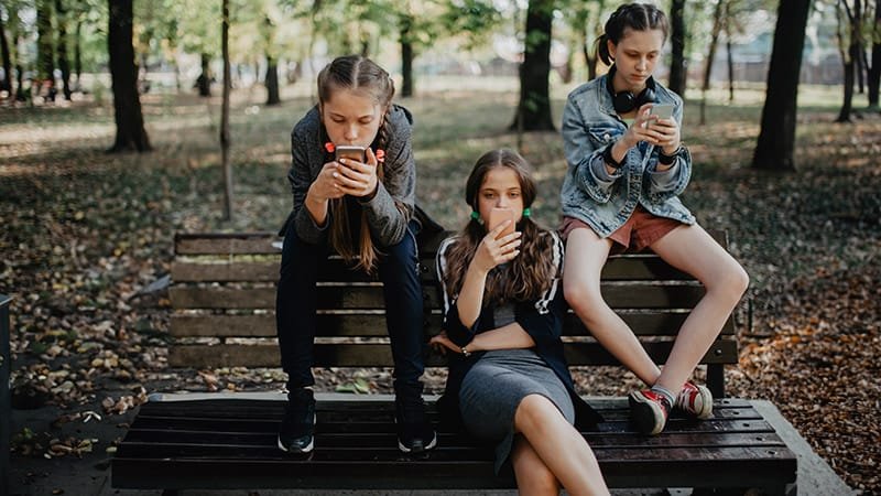 Young people sitting on a park bench addicted to scrolling on their phones needing to fix brain fog in 2026
